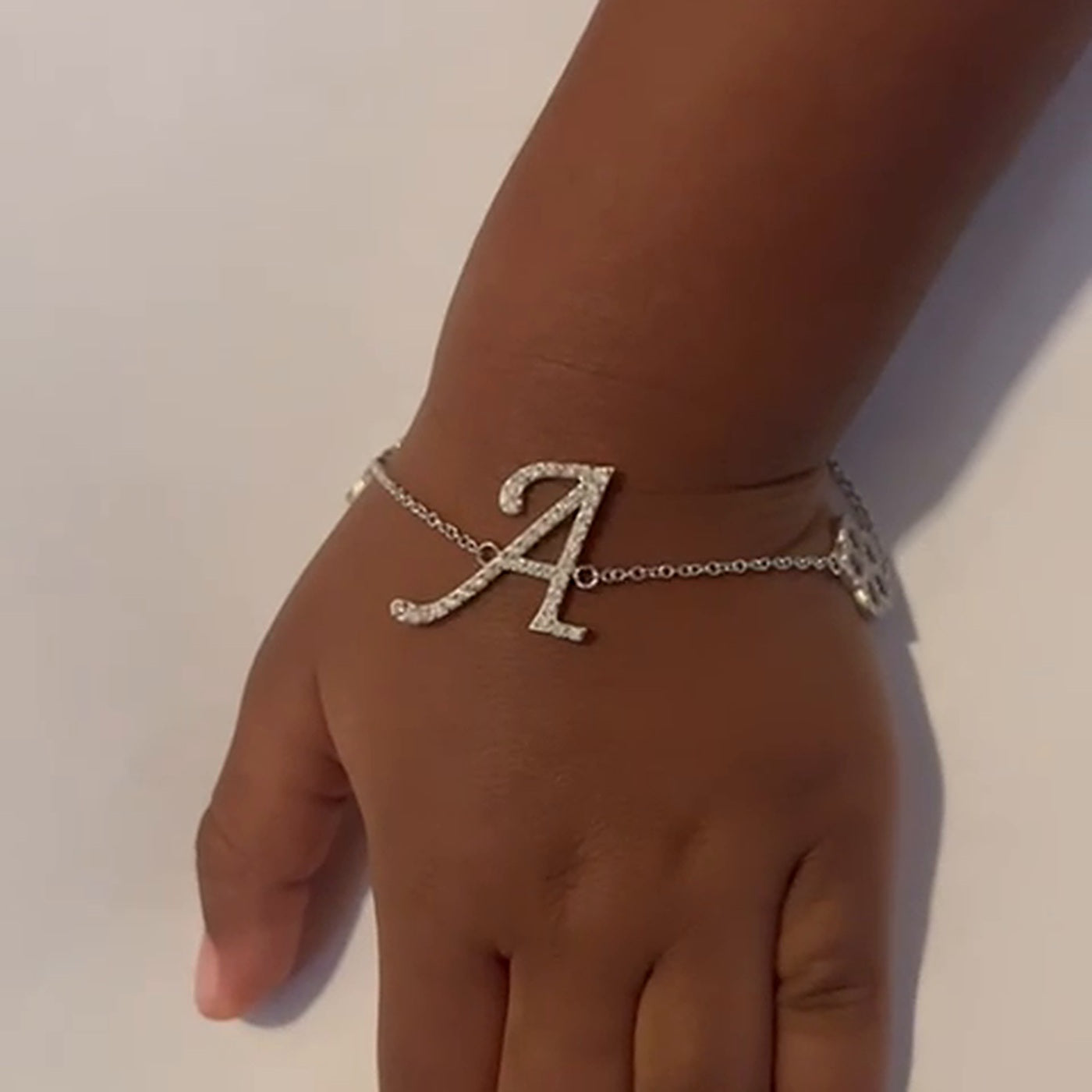 Diamond script initial bracelet with flower charm, worn by a child
